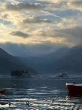 Seagulls swim in the sea near a fishing boat against the backdrop of mountains and sunset. High quality photo
