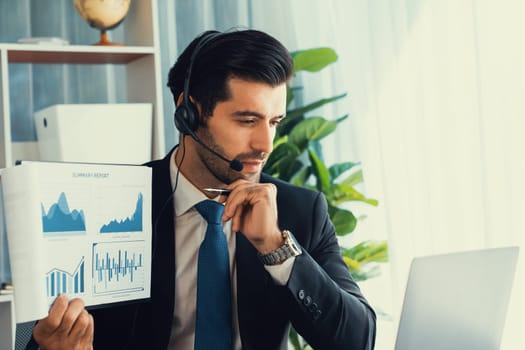 Business man wearing headphone present financial data or BI paper via laptop during online meeting. Remote work concept with virtual meeting presentation of effectiveness remote work. Fervent