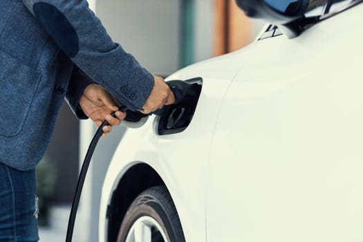 Closeup progressive asian man install cable plug to his electric car with home charging station. Concept of the use of electric vehicles in a progressive lifestyle contributes to clean environment.