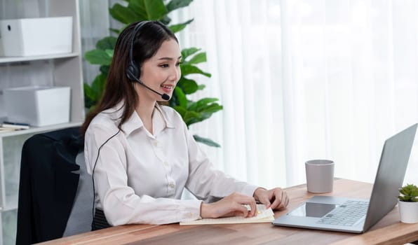 Asian call center with headset and microphone working on her laptop. Female operator provide exceptional customer service. Supportive call center agent helping customer on inquiry. Enthusiastic