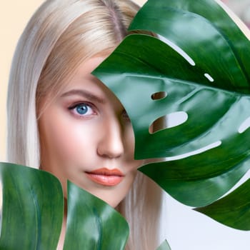 Closeup facial portrait personable woman with perfect smooth makeup holding green monstera leaves and cover her face as natural healthy skincare treatment. Tropical nature and beauty concept