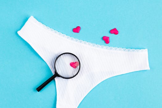 heart lies under a magnifying glass of women's panties, among many other hearts on light blue background. concept of searching for lover, find lover. Love background. romantic minimalism background.