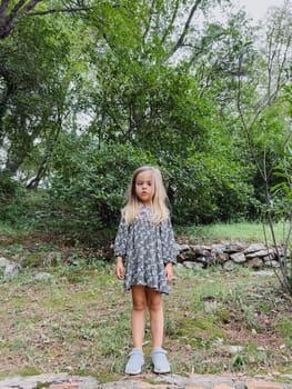 Little girl in a dress and sneakers stands in a green park. High quality photo