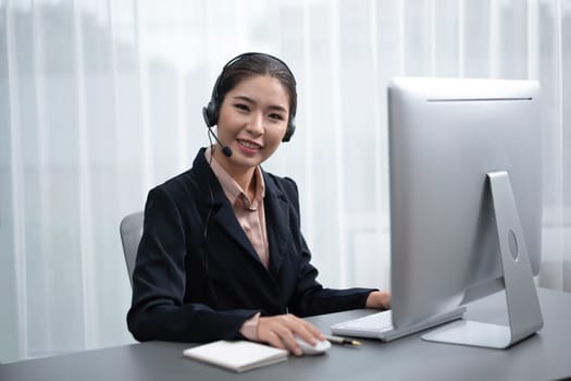 Asian call center with headset and microphone working on her workspace looking at camera. Female operator provide exceptional customer service. Supportive call center agent portrait. Enthusiastic