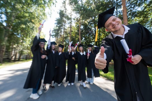 Happy young caucasian male graduate showing thumbs up. A group of graduate students outdoors