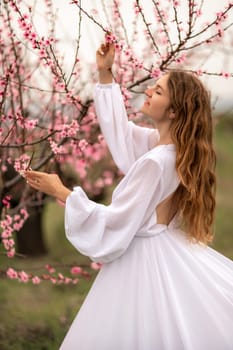 Woman peach blossom. Happy curly woman in white dress walking in the garden of blossoming peach trees in spring.