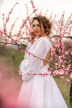 Woman peach blossom. Happy curly woman in white dress walking in the garden of blossoming peach trees in spring.