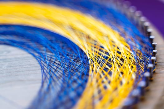 Colored thread mandala on a wooden board with nails. Mandala Moon Harmony Sun esotericism and psychology pictures from yellow and blue silk threads