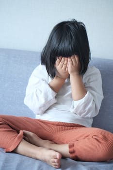 a upset child girl cover her face with hand .