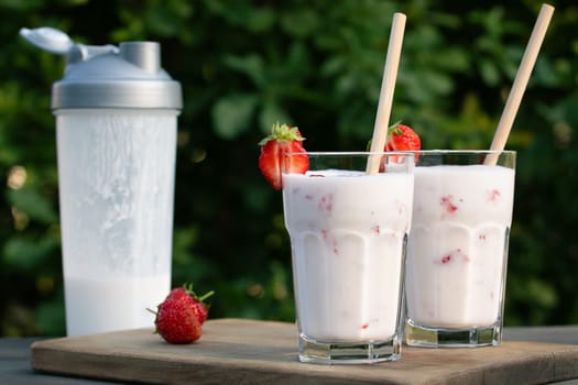 Protein shake from yogurt and strawberries in a shaker and two glass glasses on a wooden table.