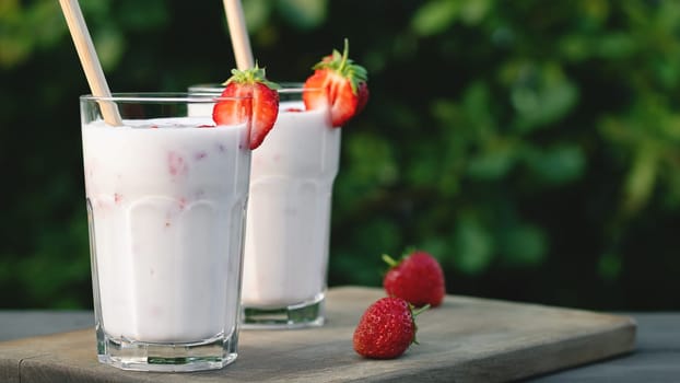 Strawberry smoothie in two glass glasses and fresh strawberries on a wooden table in the yard, copyspace.