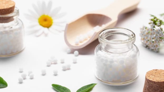 Composition of homeopathic medicines and medicinal plants on a white table.