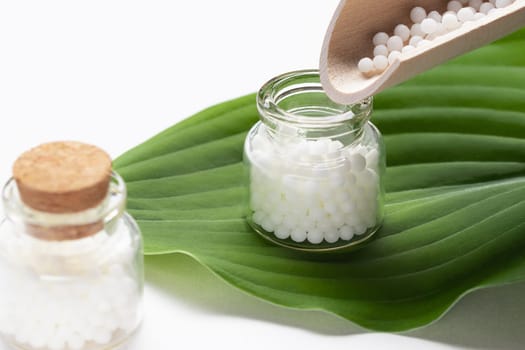 Pouring homeopathic granules from a wooden scoop into a bottle.