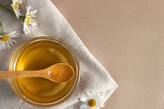 Chamomile syrup in a small bowl and in a jar and chamomile flowers on a linen kitchen towel, copy space.