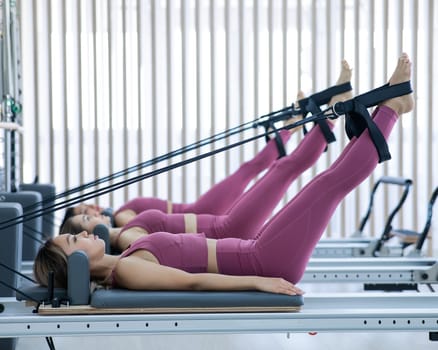 Three Asian women in pink sportswear doing pilates exercises with a reformer bed