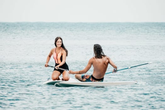 Sea woman and man on sup. Silhouette of happy young woman and man, surfing on SUP board, confident paddling through water surface. Idyllic sunset. Active lifestyle at sea or river