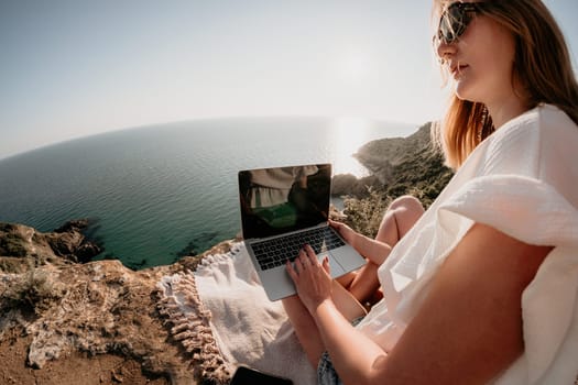 Woman sea laptop. Business woman in yellow hat working on laptop by sea. Close up on hands of pretty lady typing on computer outdoors summer day. Freelance, digital nomad, travel and holidays concept.