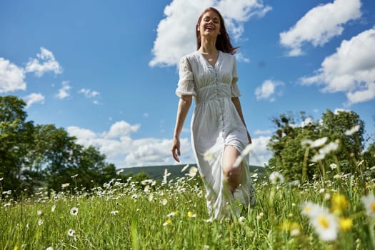 a happy woman in a light dress runs across a field of daisies towards the camera. Sunny weather, peace, happiness. High quality photo