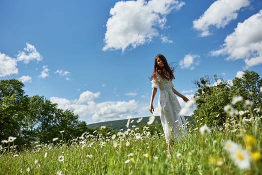 a happy woman in a light dress runs across a field of daisies towards the camera. Sunny weather, peace, happiness. High quality photo