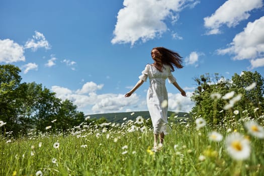 a woman in a long light dress with hair covering her face in a chamomile field against a blue sky with clouds. High quality photo