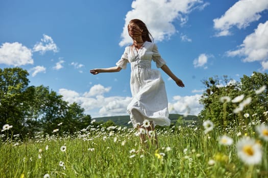 a woman in a long light dress with hair covering her face in a chamomile field against a blue sky with clouds. High quality photo