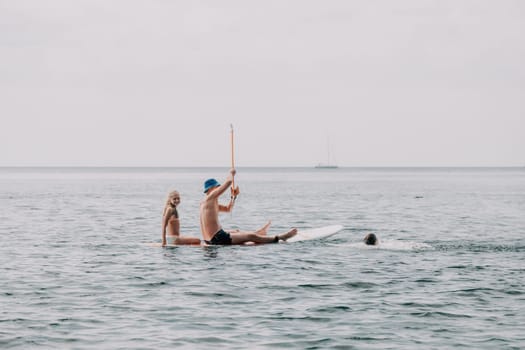 Father and his adorable little son and daughter sitting on stand up board having fun during summer beach vacation