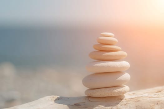 Pyramid stones on the seashore with warm sunset on the sea background. Happy holidays. Pebble beach, calm sea, travel destination. Concept of happy vacation on the sea, meditation, spa, calmness.