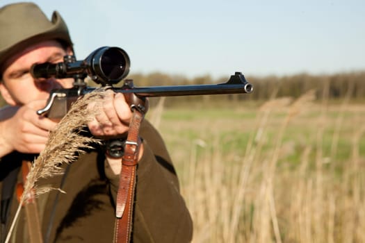 Hunting, gun and man on a Africa safari in the grass for shooting animals on holiday. Weapon, sniper and male person aim for wild game in nature with mockup and scope for target shot in the sun.