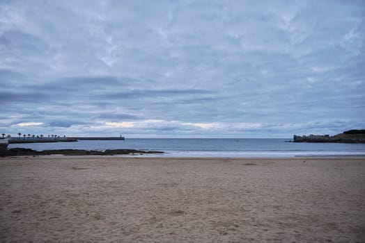 Beach of Castro Urdiales in Spain, cloudy day. No people, sand, clouds, clouds, sunset, lighthouse breakwater rocks palms