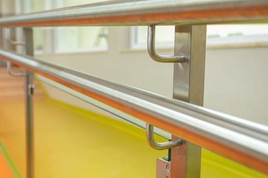 Close-up view of the installed handrail with a round section to a post with a plugged profile and a square section. The components are made of stainless steel.