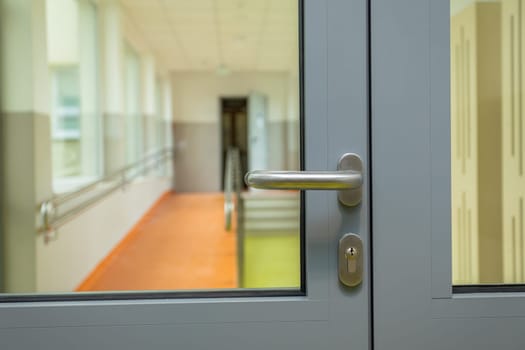Corridor rooms divided by an aluminum door with glass. View of a section of the door with a saloon-colored handle.