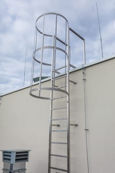 Stainless steel ladder attached to the wall outside the building. Technical access to the higher part of the roof.