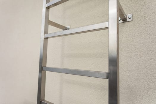 Close-up view of a section of a stainless steel ladder mounted on a building wall. Square stainless steel section.