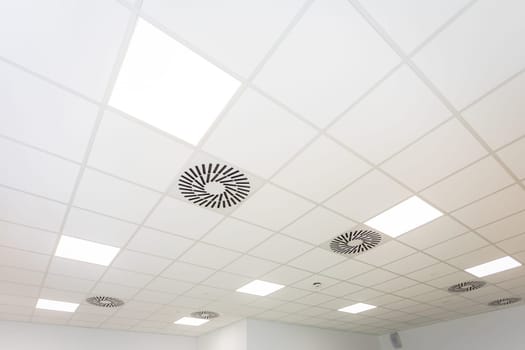 Lamps shine in the suspended ceiling and the whole thing seen from below and with perspective. Modern and fashionable panel ceiling in a large room.