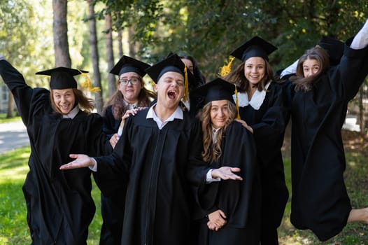 A group of graduates in robes congratulate each other on their graduation outdoors