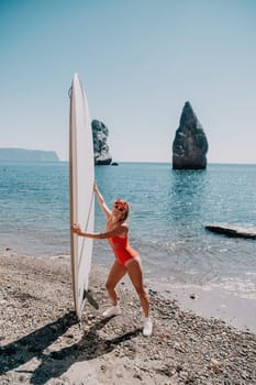 Close up shot of beautiful young caucasian woman with black hair and freckles looking at camera and smiling. Cute woman portrait in a pink bikini posing on a volcanic rock high above the sea