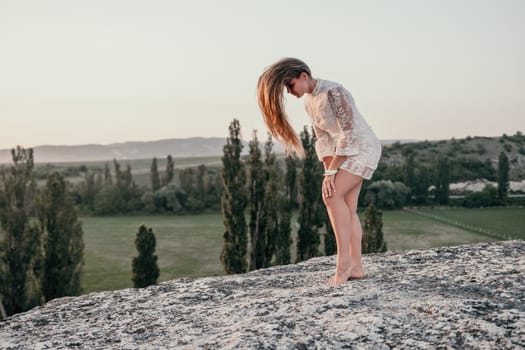 Romantic beautiful bride in white dress posing with sea and mountains in background. Stylish bride standing back on beautiful landscape of sea and mountains on sunset