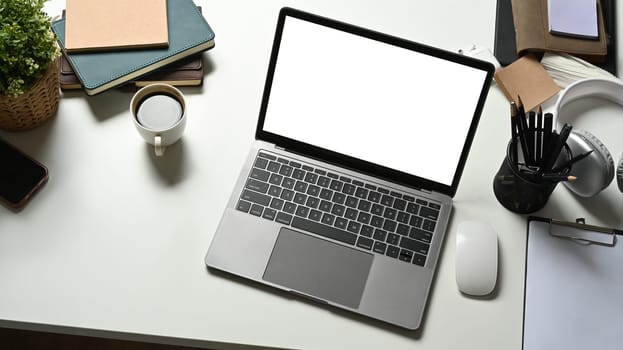 A laptop computer, coffee cup and supplies on white office desk. Blank screen for your advertising text message.