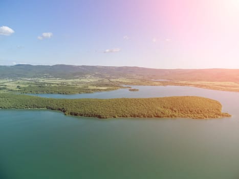 Aerial landscape from flying drone storage reservoir at mountain foot covered colorful spring forest. Beautiful view from above blue lake among highlands