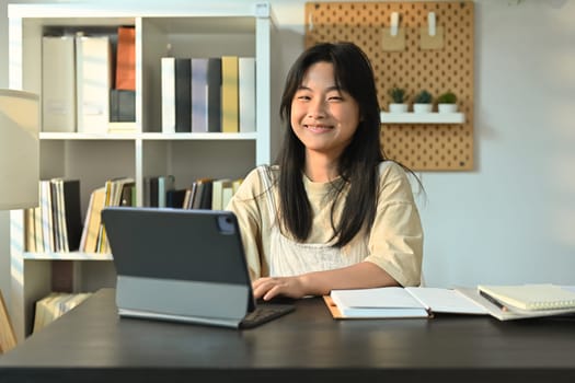 Smiling teenage girl studying online classes on digital tablet at home. Online learning, homeschooling concept.