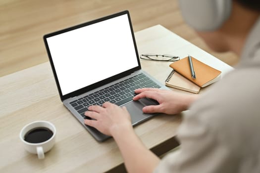 Male freelancer using laptop with blank empty mockup screen on couch at home, watching webinars, working remotely.