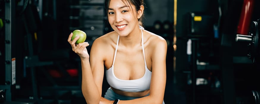 A female runner holds a green apple in a gym, reminding viewers of the importance of healthy food choices for achieving fitness goals. Healthy fitness and eating lifestyle concept