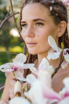 Magnolia flowers. Happy woman enjoys by blooming magnolia tree and sniffs it flowers with closed eyes in spring garden. Portrait