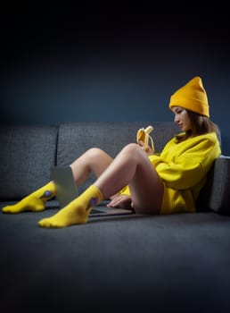 sexy girl in yellow clothes and a hat with a banana and a laptop on dark background copy paste