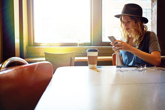 Texting everyone to check out this coffee shop. a female hipster in a coffee shop