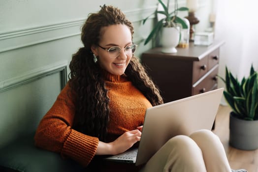 Young woman enjoying online shopping and elearning on laptop at home. Home shopping and elearning with a happy woman using laptop on sofa