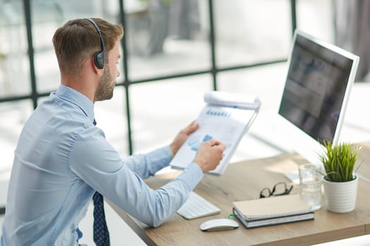 Young handsome male customer support phone operator with headset working in his office