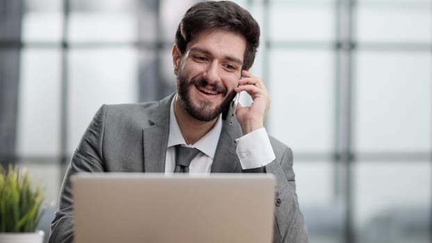 Smiling man while making phone call and using laptop in the office