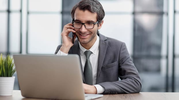 Happy young businessman talking on smart phone at desk in office