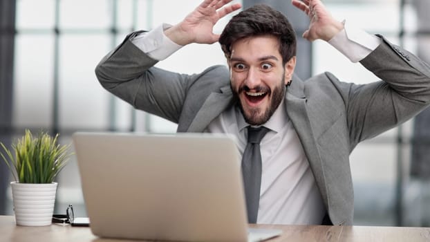 Excited businessman sitting at table with laptop and celebrating success